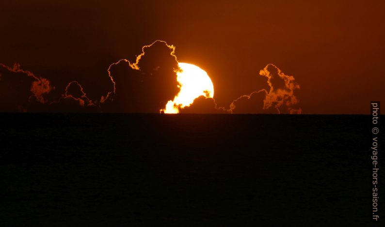 Le cercle du soleil plonge dans l'horizon derrière des nuages. Photo © André M. Winter