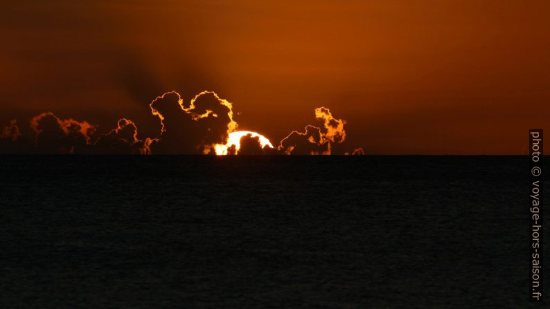 Le cercle du soleil plonge derrière des nuages. Photo © André M. Winter