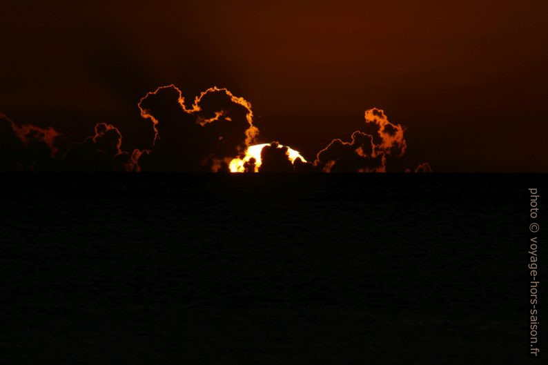 Le cercle du soleil plonge derrière des nuages. Photo © André M. Winter