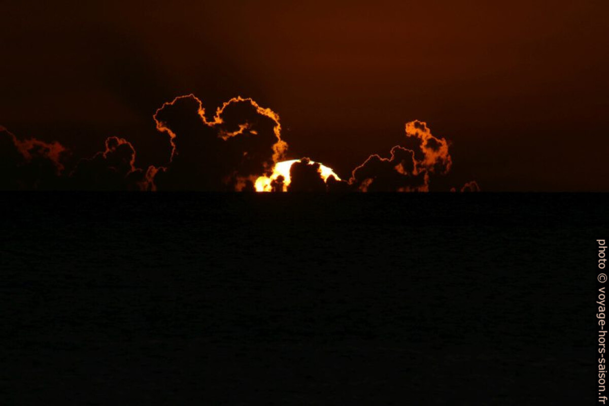 Le cercle du soleil plonge derrière des nuages. Photo © André M. Winter