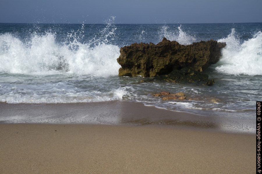 Vague qui éclate derrière un rocher sur la plage. Photo © André M. Winter
