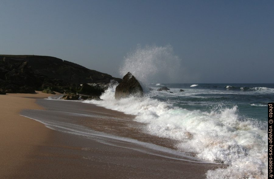 Une vague arrive sur la plage et éclate contre un rocher. Photo © André M. Winter